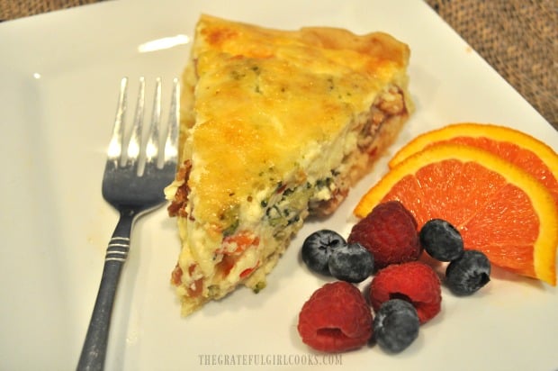 One slice of bacon broccoli quiche, with fresh fruit on the side.