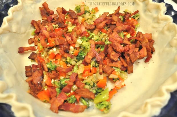 The cooked bacon and veggies are added to an uncooked pie crust.