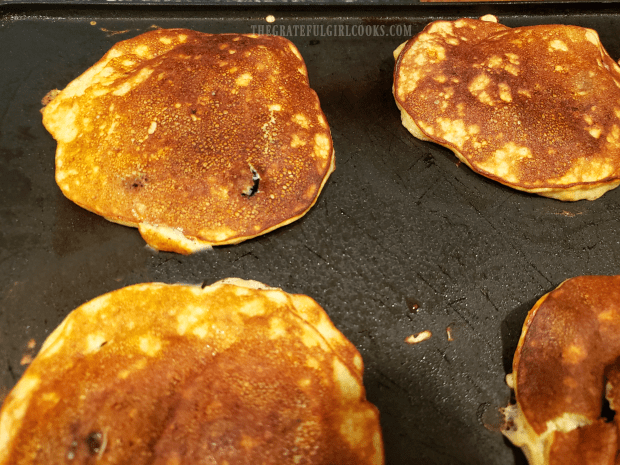 The banana blueberry pancakes are carefully flipped to cook other side.