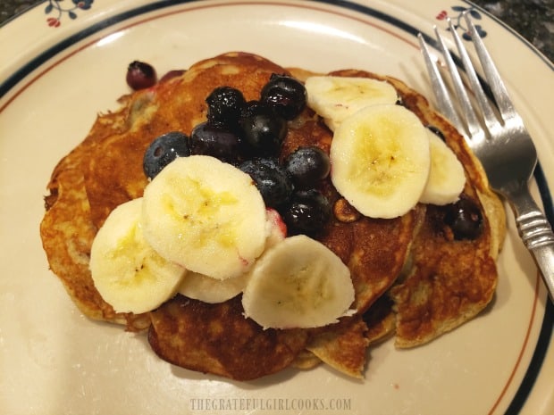 A serving of banana blueberry pancakes, topped with banana slices and fresh blueberries.