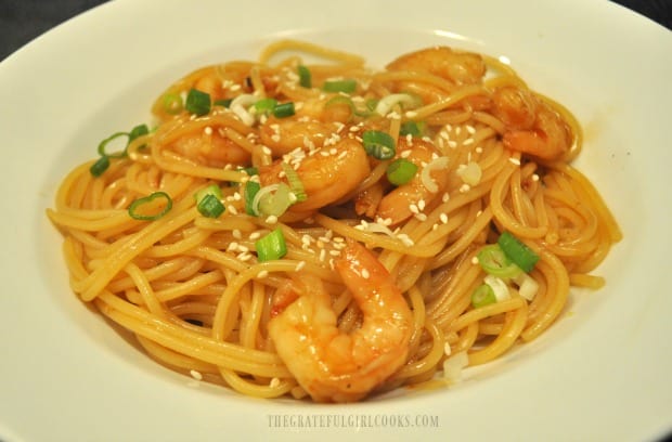 The sweet chili shrimp pasta is served, topped with sesame seeds and green onions.