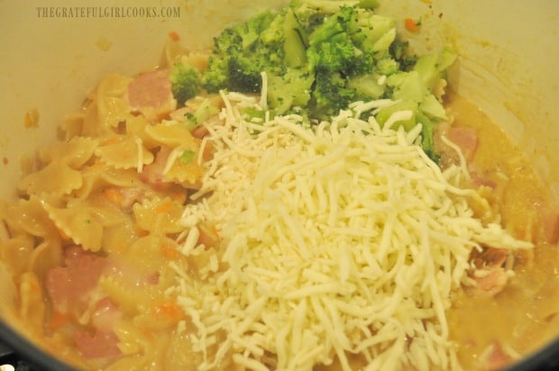 Cooked broccoli, mozzarella and Parmesan cheeses are added to the saucepan.