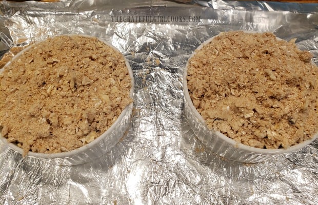 A streusel topping is placed on top of the sugar-coated blueberries in ramekins before baking.