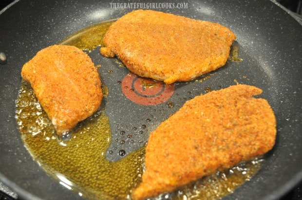 The cornmeal spice-crusted rockfish fillets are cooked in canola oil in a skillet.