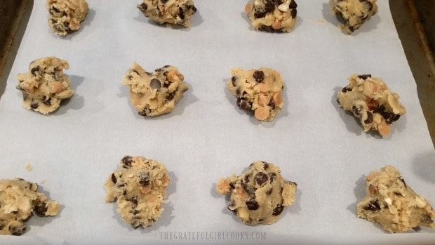 Cookie dough is dropped by spoonfuls on parchment paper lined cookie sheet.