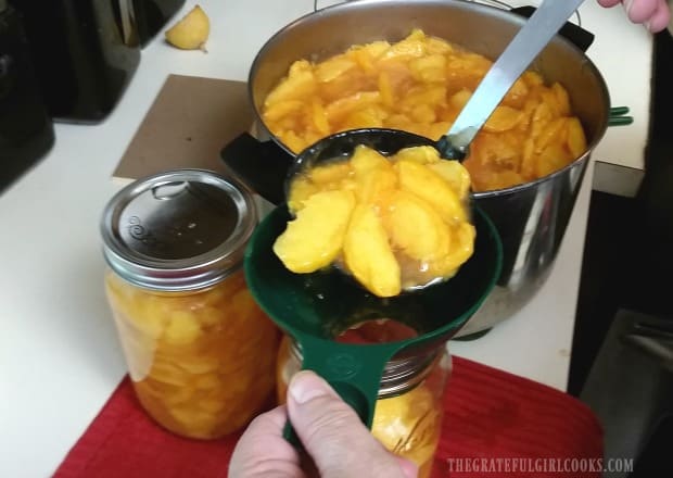 The peach pie filling is ladled into the hot canning jars.
