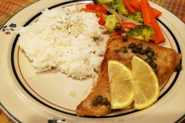 The lemon piccata cod is topped with lemon slices, and served with rice and veggies.