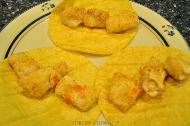 A few pieces of broiled fish are placed in each corn tortilla.