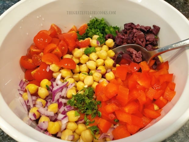 Tomatoes, bell peppers, garbanzo beans, red onion, kalamata olives & fresh herbs in bowl.