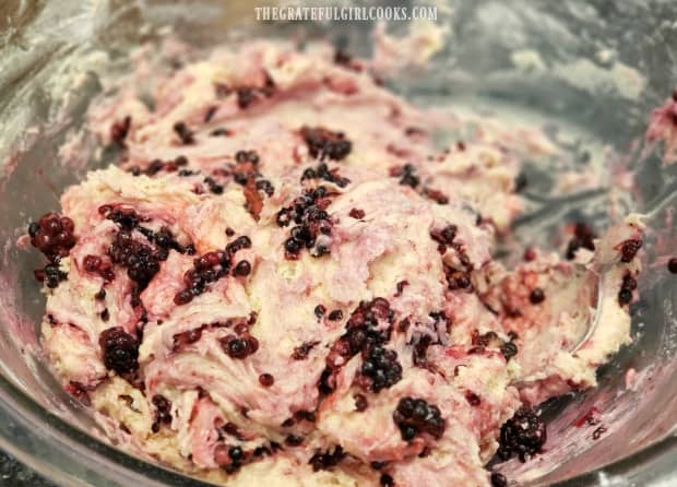 The batter for the muffins is streaked with color from the blackberries.