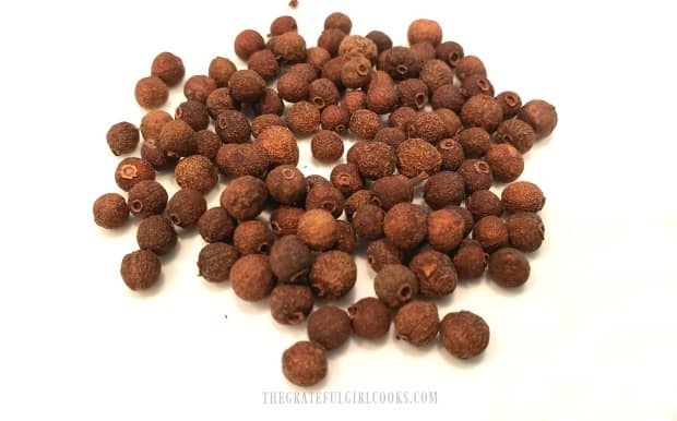 Whole, dried allspice berries on a white plate.