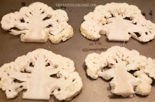 Four cauliflower steaks are placed onto a baking sheet.