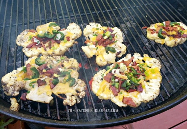 Loaded grilled cauliflower is topped with cheese, bacon, green onions, and jalapeños.