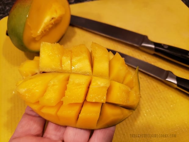 The mango is flipped to expose the cubes, and then they are cut away from the peel.