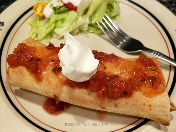 A chimichanga is served, topped with salsa and sour cream, and a side salad.