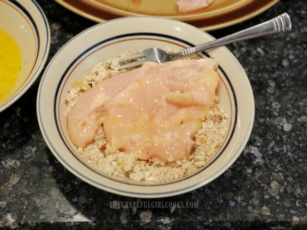Egg covered chicken breasts are dredged in bread crumbs before cooking.