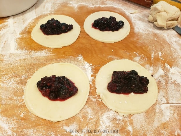 A spoonful of blackberry pie filling is placed onto each pie dough circle.
