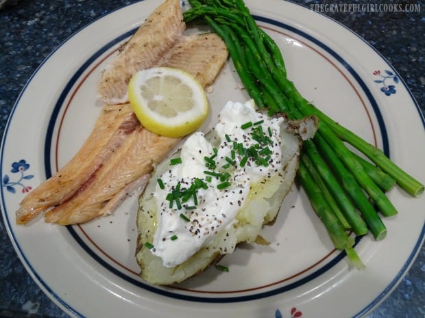 The grilled trout, on a plate with side veggies, ready to eat.