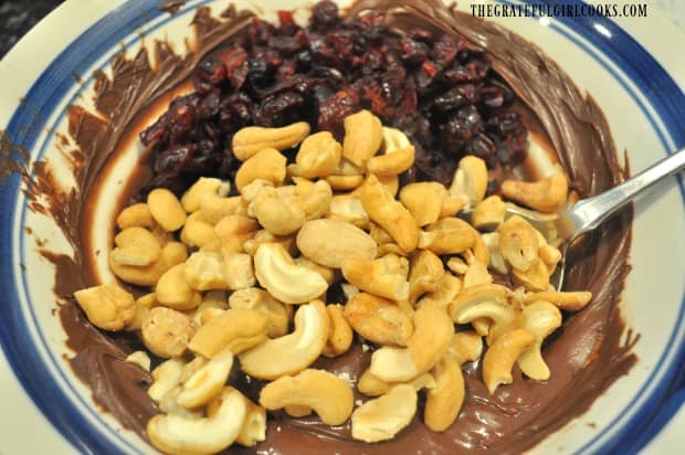 Dried cranberries and cashews are added to the melted chocolate in the bowl.