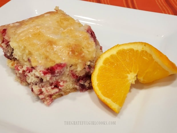 A piece of the glazed cranberry orange cake on a white plate, with orange slice.