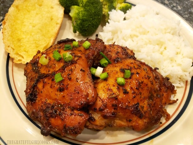 Two pieces of marinated baked chicken thighs, served with rice, bread and broccoli.