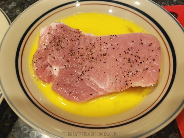 Each pork chop is immersed in egg mixture, to cover.