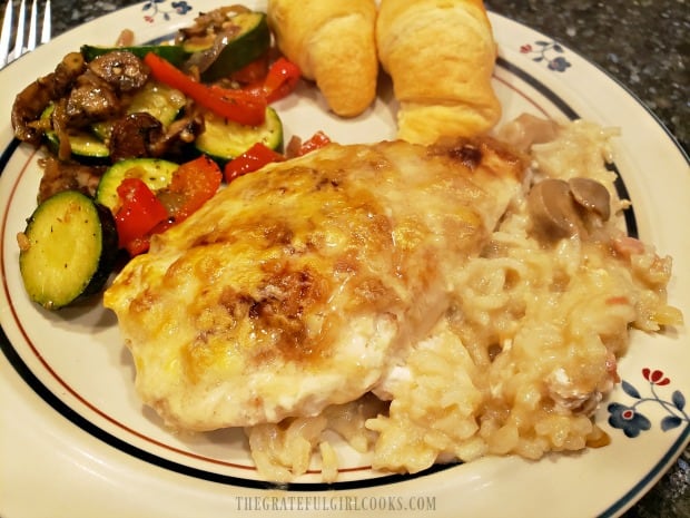 Easy chicken rice casserole is served on plate, with vegetables and rolls.