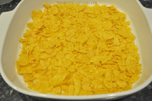 Corn tortilla chips are crushed and placed in baking dish.