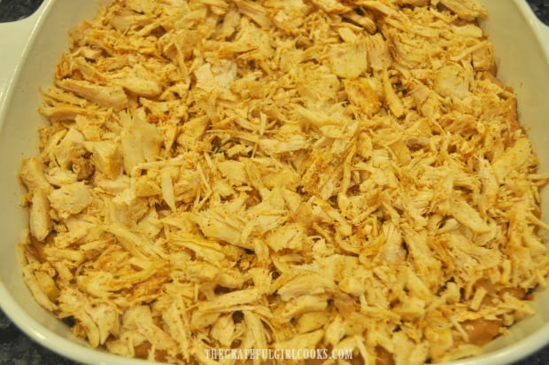 Seasoned shredded turkey is placed on top of refried bean mixture in casserole dish.