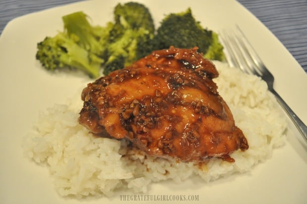 Chicken thigh with sauce is served on steamed rice, with broccoli on the side.