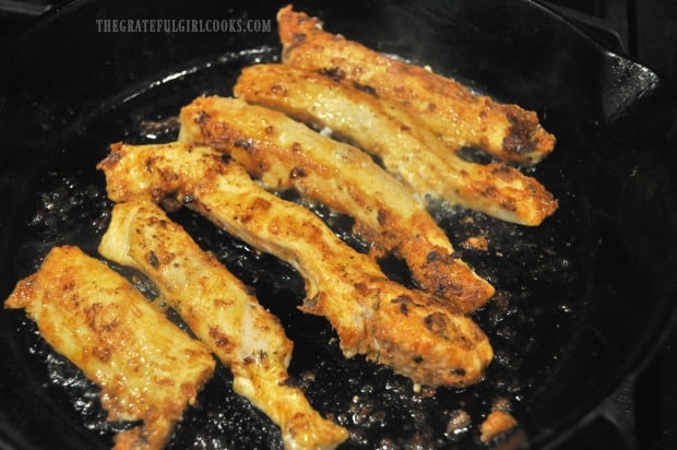 The chicken strips are flipped to cook the other side after browning.