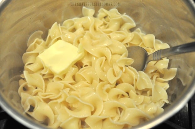 Egg noodles are cooked, drained, then buttered before topping with stroganoff.