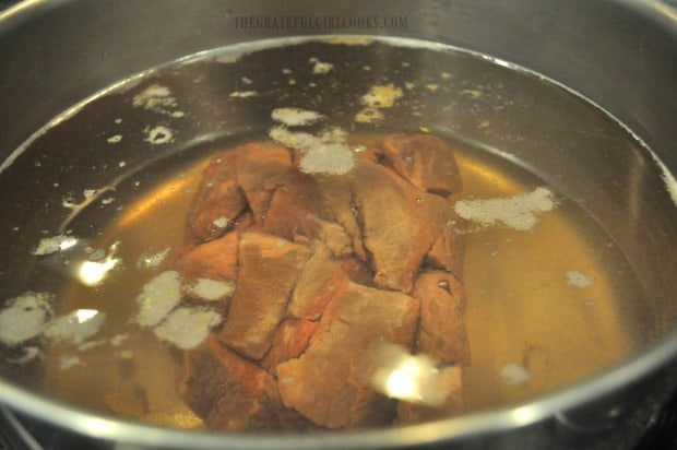 Stew meat is cooked in beef broth in a large stock pot.