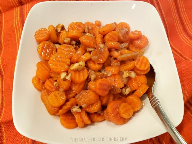 The orange glazed carrots with pecans are served in a white bowl.