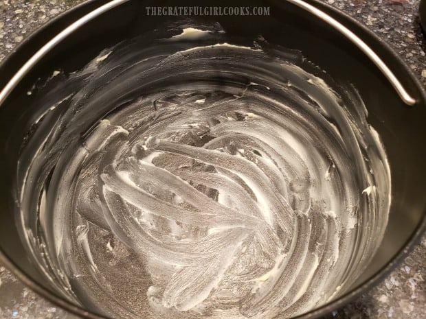 A 7" round pan is coated with butter before adding brownie batter.