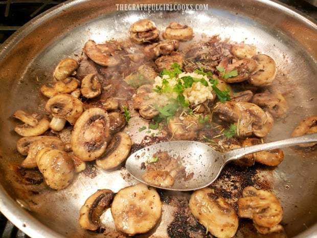 Garlic and herbs are added to the cooked mushrooms in skillet
