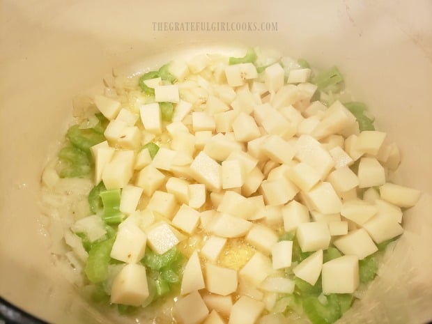 Cubed raw potatoes are added to onions, celery and butter in pan to cook and soften.