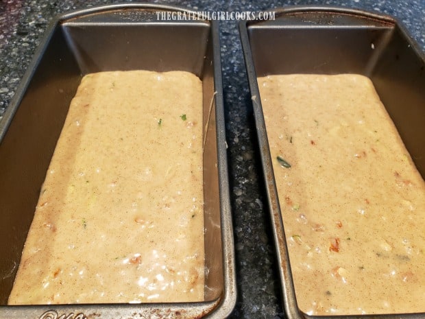 Zucchini nut bread batter is evenly divided into 2 greased loaf pans to bake.