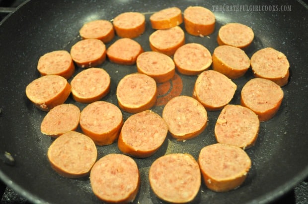 Kielbasa slices are cooked in a large skillet in a single layer.