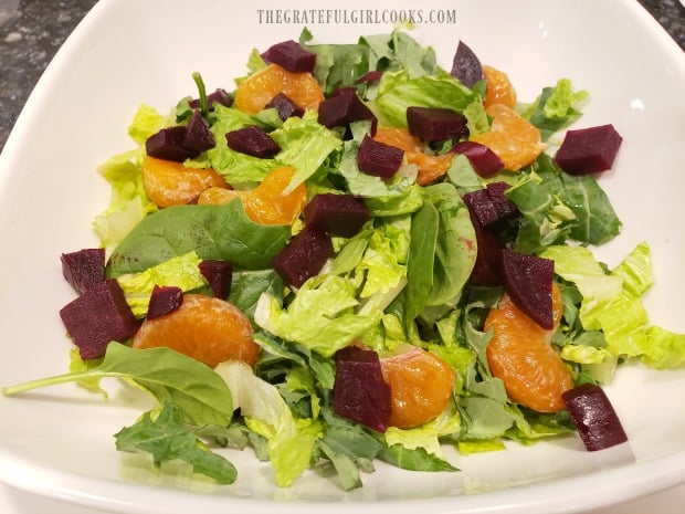 Spring greens in bowl are topped with chopped beets and mandarin oranges.