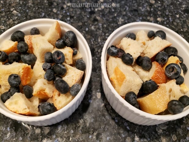 Bread cubes and fresh blueberries are placed into well-buttered ramekins.