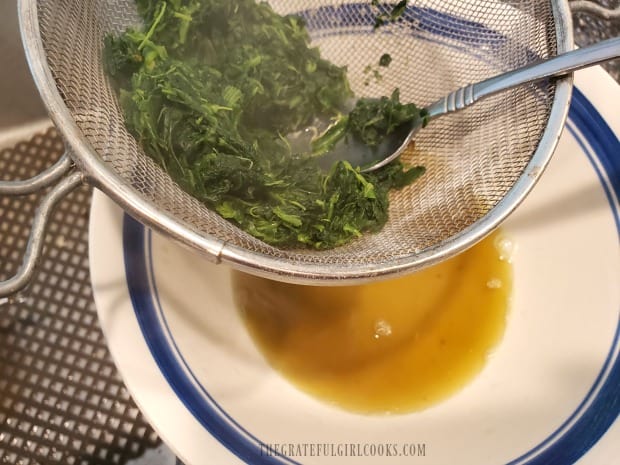 All the liquid is pressed out of the cooked spinach using a strainer.
