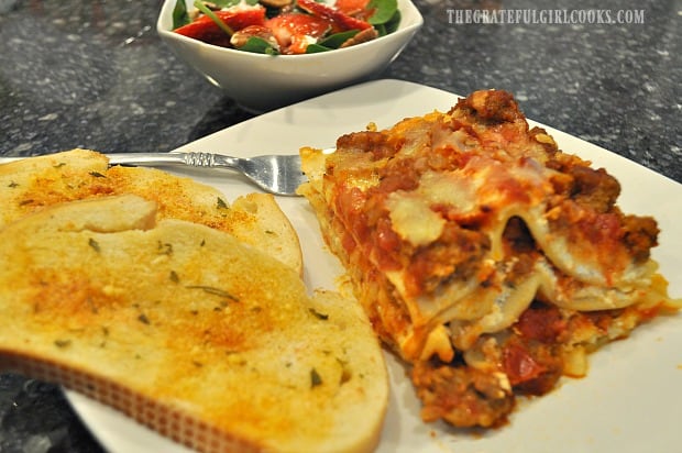 A piece of homemade lasagna served with green salad and garlic bread on the side.