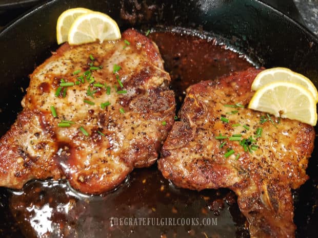Brown sugar pork chops are garnished with chives and lemon wedges before serving.