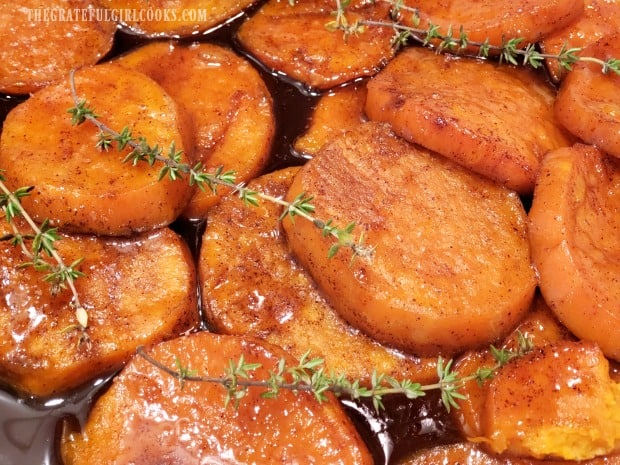 Close up of candied sweet potatoes with sprigs of fresh thyme on top.