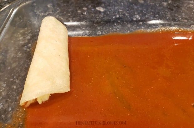 Tortillas and filling are rolled, then placed on top of enchilada sauce in baking pan.