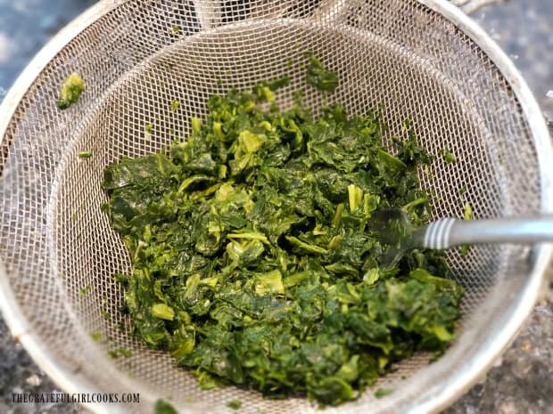 Frozen chopped spinach is thawed, then drained of excess liquid in a strainer.