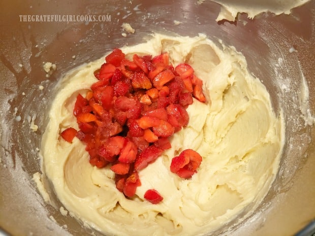 Chopped fresh strawberries are added to the bowl of muffin batter.