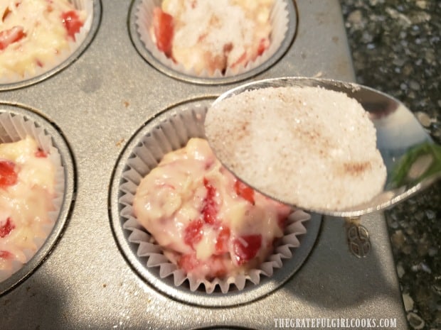 A cinnamon sugar mixture is sprinkled over top of fresh strawberry muffins before baking.