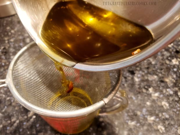 The olive oil is strained into a cup to remove any small crispy garlic pieces.